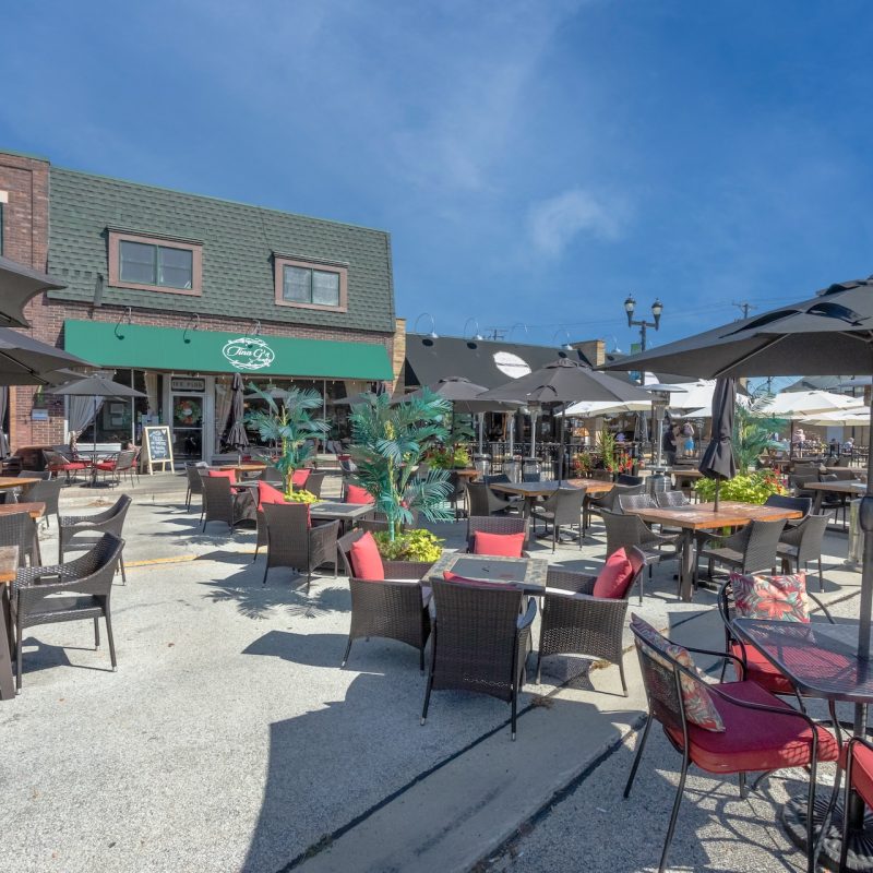 Outdoor restaurant patio dining with red cushioned chairs, patio umbrellas, and brick building in downtown Mundelein near Station 250 apartments IL